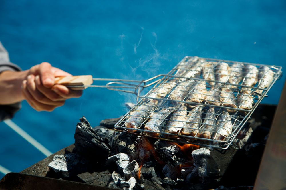 grilling fresh sardines over charcoal by the sea