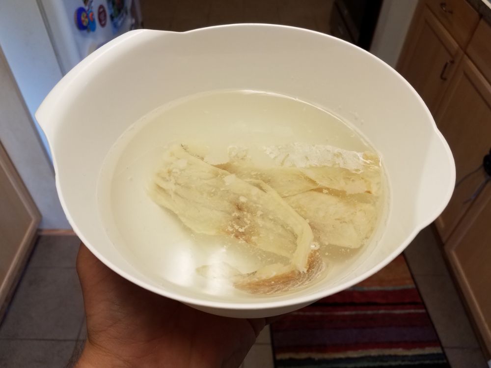 Pieces of bacalhau soaking in water in a white bowl